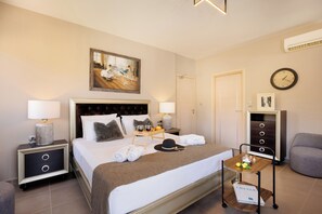 A hotel room with a large bed, bedside tables, a nightstand, a desk with a chair, a lamp, a clock, and a painting on the wall. - Lamon (Agios Vasileios)