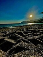 Une plage où le soleil se couche sur l’océan, projetant des ombres sur le sable.