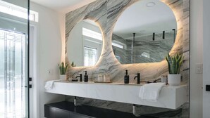 Un baño moderno con tocador de mármol, dos lavamanos, un espejo grande y una cabina de ducha de vidrio.