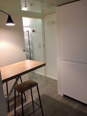 A kitchen with a wooden table and bar stool, a white refrigerator, and a door leading to another room. - In the heart of the Marais (Paris)