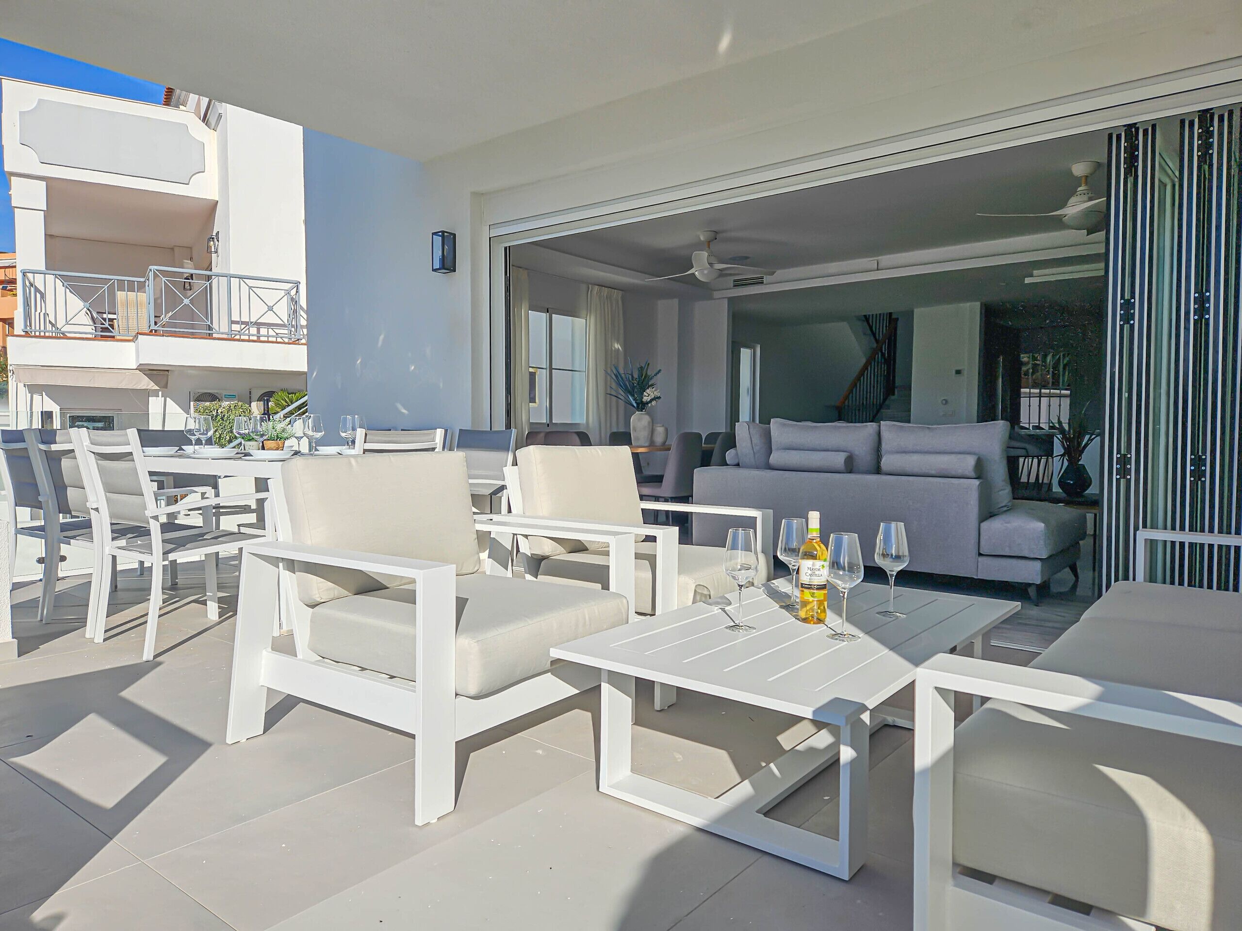 Une terrasse extérieure moderne, aménagée avec des meubles blancs, notamment des canapés et des fauteuils, ainsi qu’une table à manger.