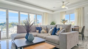 Ett modernt vardagsrum med en grå soffa, ett soffbord i trä och utsikt över staden genom stora fönster.