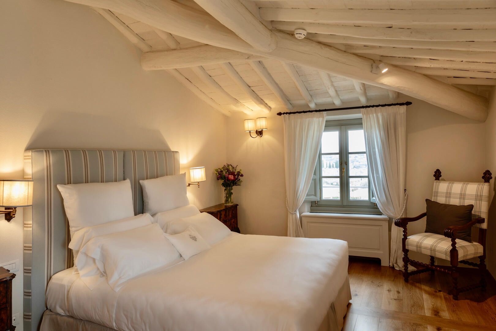 Una camera da letto con un letto grande, una sedia, una finestra con tende e una lampada.
