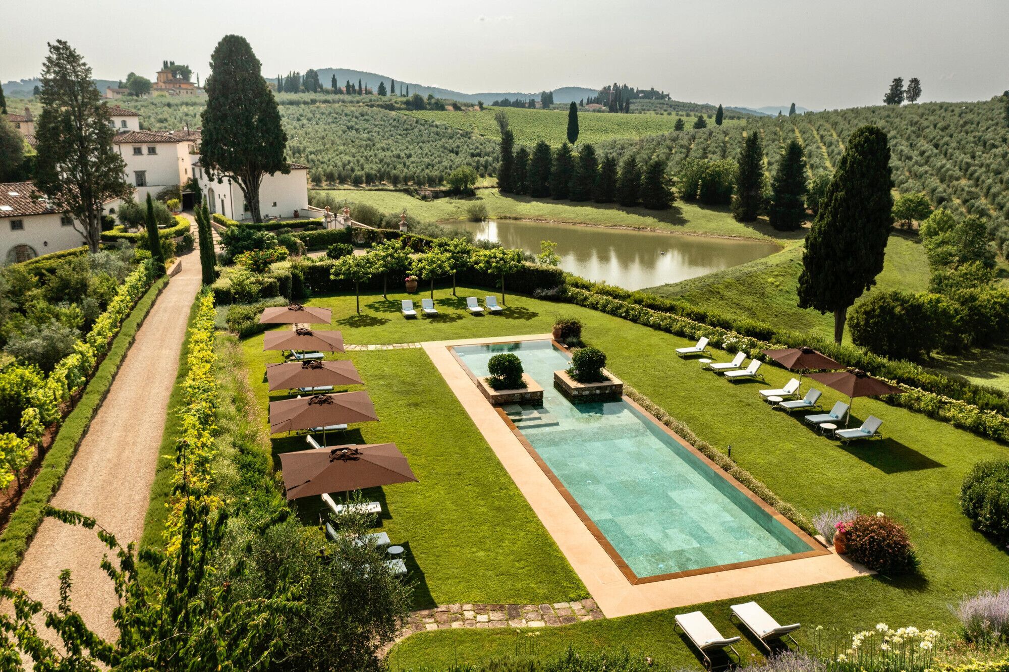Area piscina con lettini e ombrelloni, circondata da prati curati e un lago.
