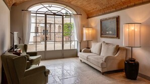 A room with a stone ceiling, a large arched window, a beige sofa, two lamps, and a framed painting. - VILLA ARTIUM - Twenty Bedroom Villa, Sleeps 37 (Firenze)