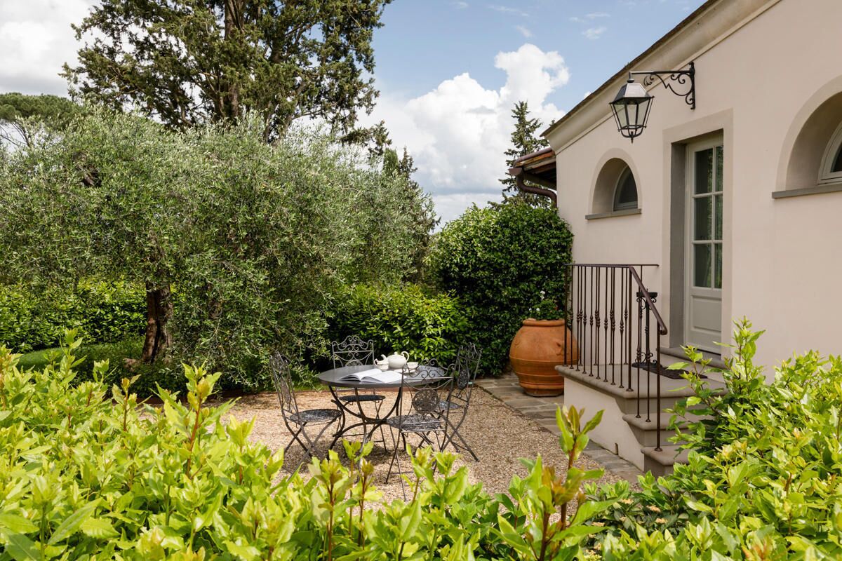 Une terrasse avec une table et des chaises, entourée d’une végétation luxuriante et donnant sur un bâtiment doté d’un balcon.