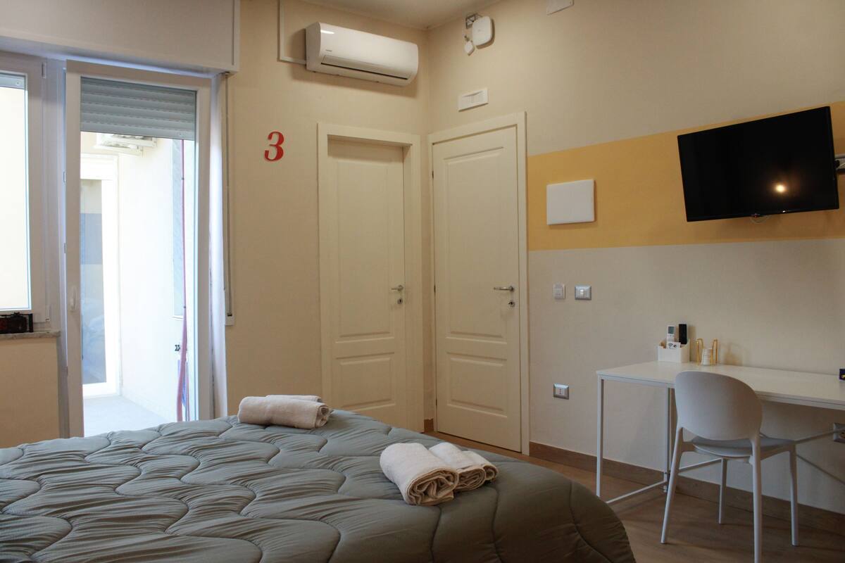 Habitación de hotel con cama, escritorio, silla, aire acondicionado, televisor y puerta con un número.