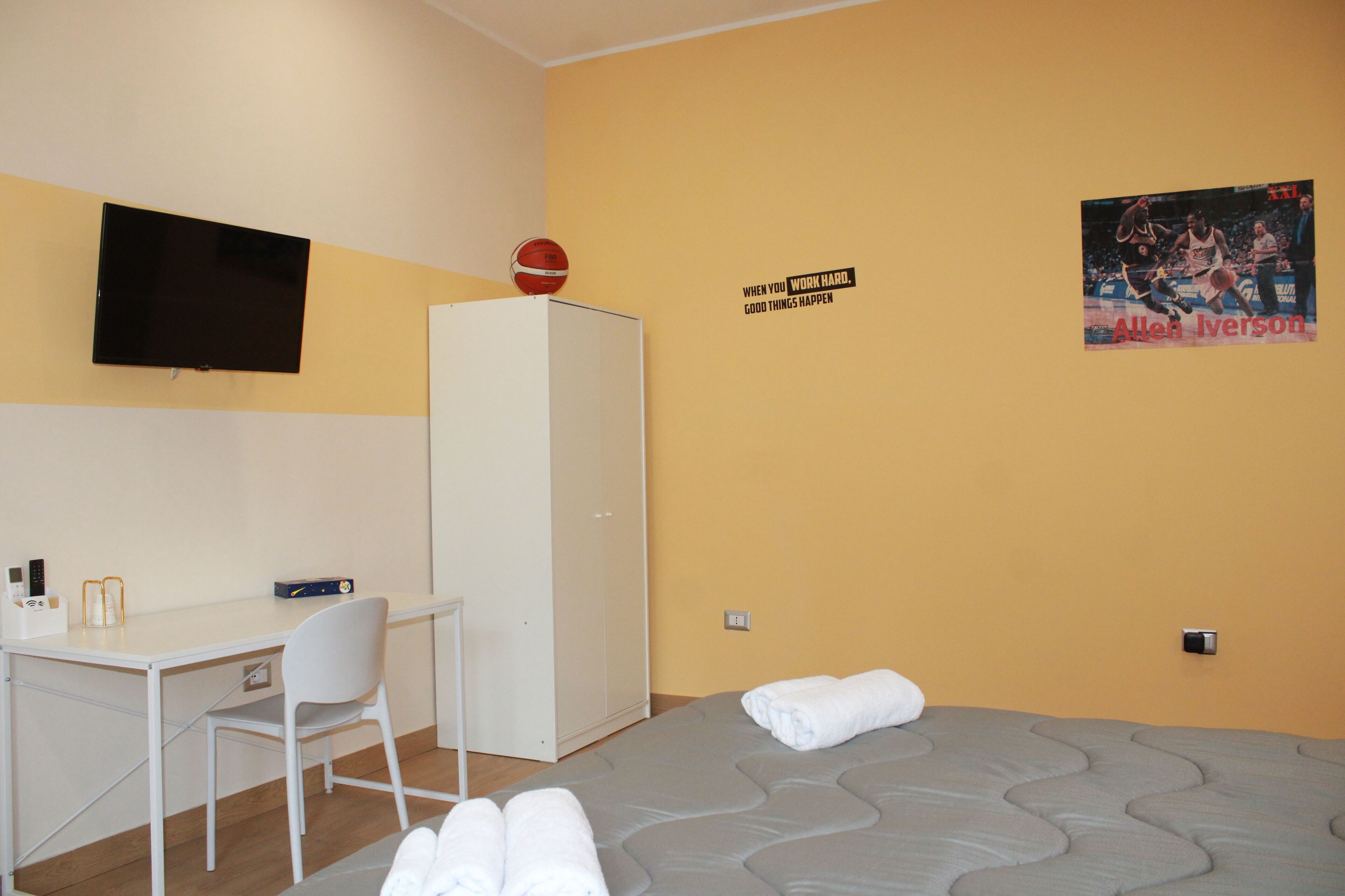 Habitación de hotel con cama, escritorio, silla, armario, televisor y un cartel en la pared.