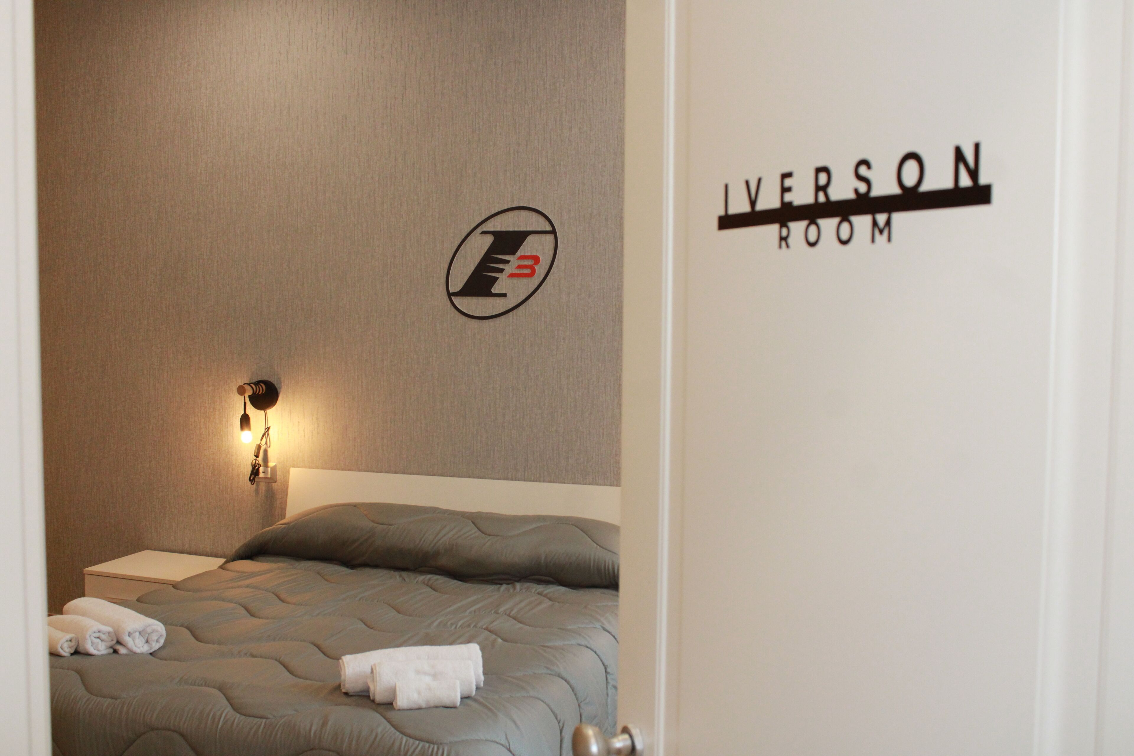 Habitación de hotel con una cama, una lámpara fijada a la pared y un letrero que dice 'LIVERSON ROOM'.