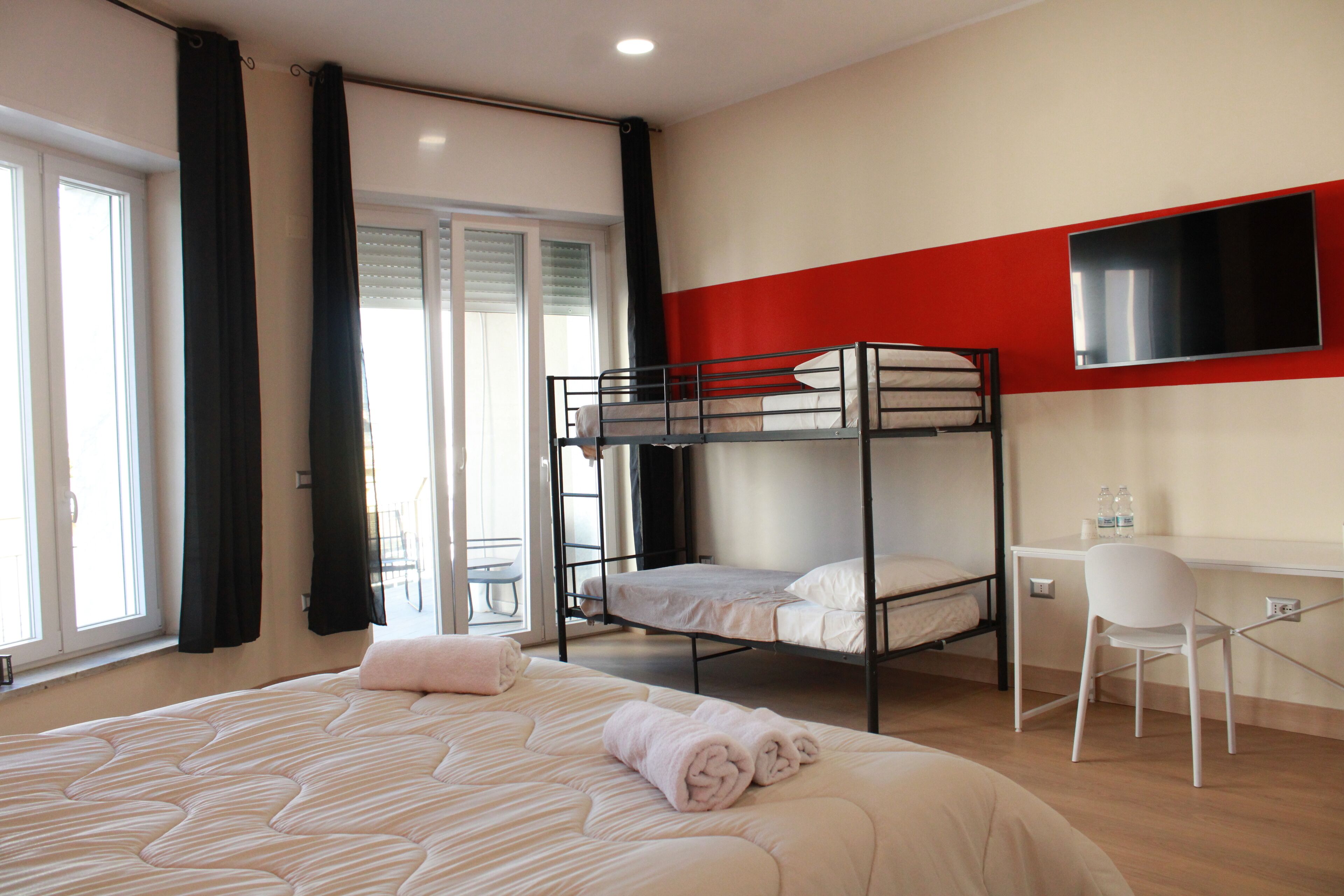 Une chambre d’hôtel avec un grand lit, un lit superposé, un bureau avec une chaise et un téléviseur fixé au mur.