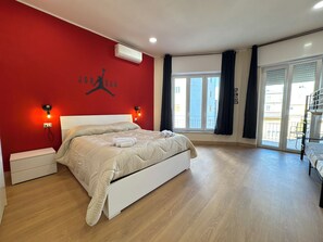 Camera da letto con parete rossa, letto bianco e finestra vista sugli edifici.