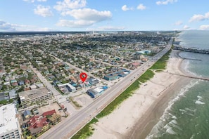 Luftaufnahme einer Küstenstadt mit Strand, einem markierten Ort und einer Straße parallel zum Ufer.
