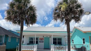 A turquoise two-story building with a teal porch and a green door, numbered 3116. - Coral Bungalow (Galveston)