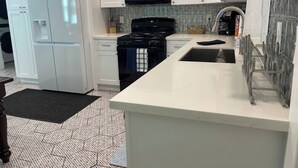 A kitchen with white cabinets, a black stove, a microwave, and a refrigerator. - Coral Bungalow (Galveston)