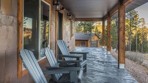 Eine überdachte Veranda mit Adirondack-Stühlen und Steinboden, mit Blick auf einen bewaldeten Bereich.