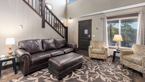 Ein Wohnzimmer mit einem braunen Ledersofa, passendem Hocker, einem gemusterten Teppich und zwei gemusterten Sesseln. Im Hintergrund ist eine Treppe zu sehen.