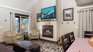 Ein Wohnzimmer mit Kamin, einem darüber montierten Fernseher und einem Essbereich mit Tisch und Stühlen.