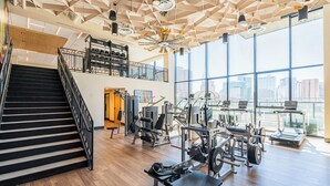 A gym with a staircase, exercise equipment, and large windows offering a city view. - 1117 Saiya  (Phoenix)