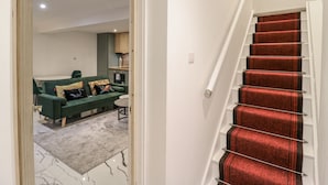 A staircase with red carpet, a green sofa with patterned cushions, and a marble-patterned rug in a modern living area. - 2A Ruby Street (London)