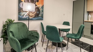 A modern dining area with a round table and green chairs, a large abstract painting on the wall, and a potted plant. - 2A Ruby Street (London)