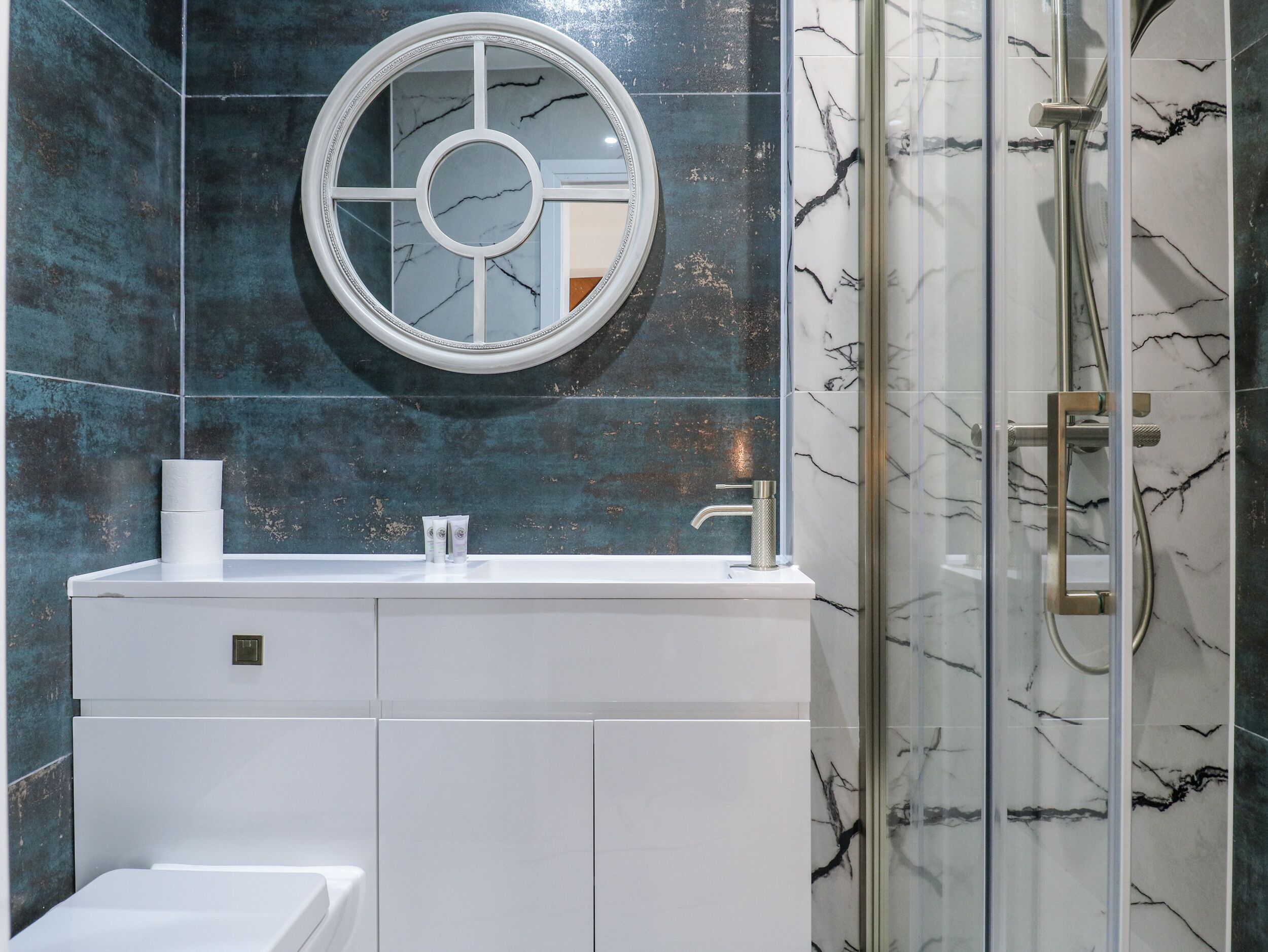 A bathroom with a white vanity, a round mirror, and a glass shower enclosure.