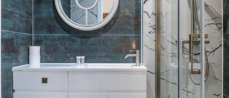 A bathroom with a white vanity, a round mirror, and a glass shower enclosure.