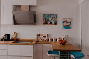 Une cuisine moderne avec des armoires blanches, un plan de travail en bois, un four encastré et un tableau représentant un cupcake.