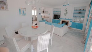 A modern kitchen with white and blue cabinetry, a dining area with wicker furniture, and a peacock decoration on the wall. - Apartment 'Melina' with Sea View, Wi-Fi and Air Conditioning (Cala del Moral)