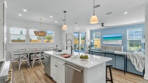 A modern kitchen with white cabinetry, a central island, pendant lighting, and a view of the outdoors. - Aquadisiac: Private heated pool, Free golf cart, 1min to beach, Game & Bunk room (Miramar Beach)