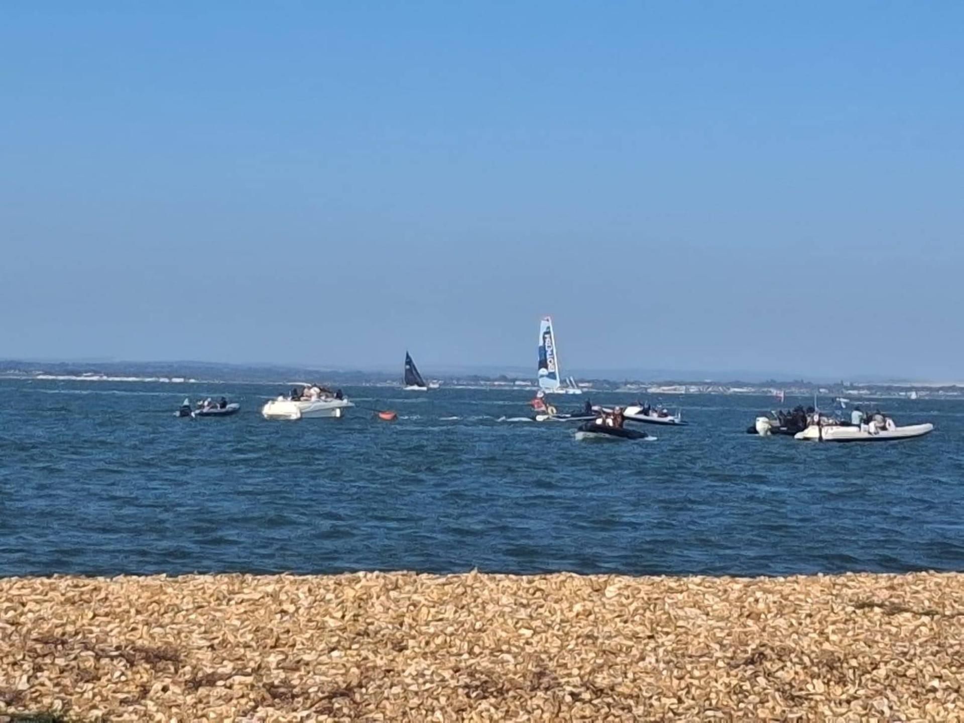 A coastal scene with boats on the water and a rocky shoreline in the foreground.