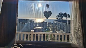 A view through a window with a white picket fence, a heart-shaped decoration, and a tree. - 2bed-cabin Sleeps 4, Wifi, Free Parking, Sea Views (Bembridge)