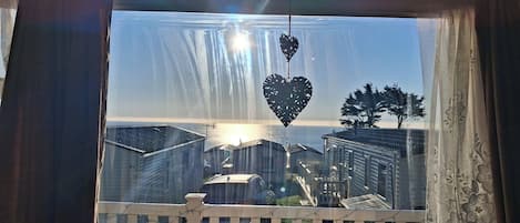 A view through a window with a white picket fence, a heart-shaped decoration, and a tree.