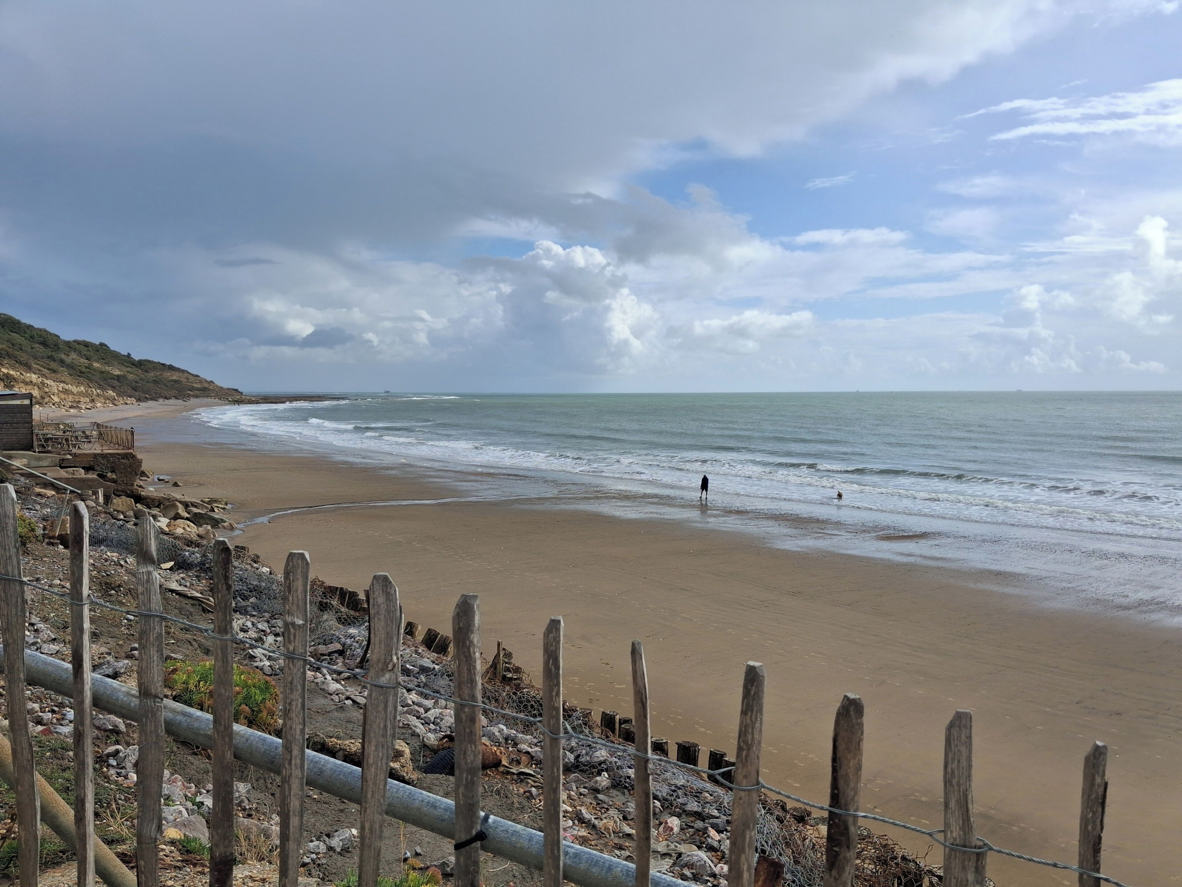 A beach with a wooden fence, rocky terrain, and a clear view of the ocean.