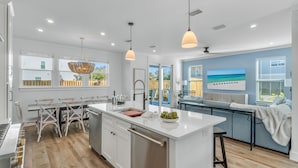 A modern kitchen with white cabinetry, a central island, pendant lighting, and a view of the outdoors. - SoCo: Private heated pool, Free golf cart, 1 min to beach, Game & Bunk rooms (Miramar Beach)