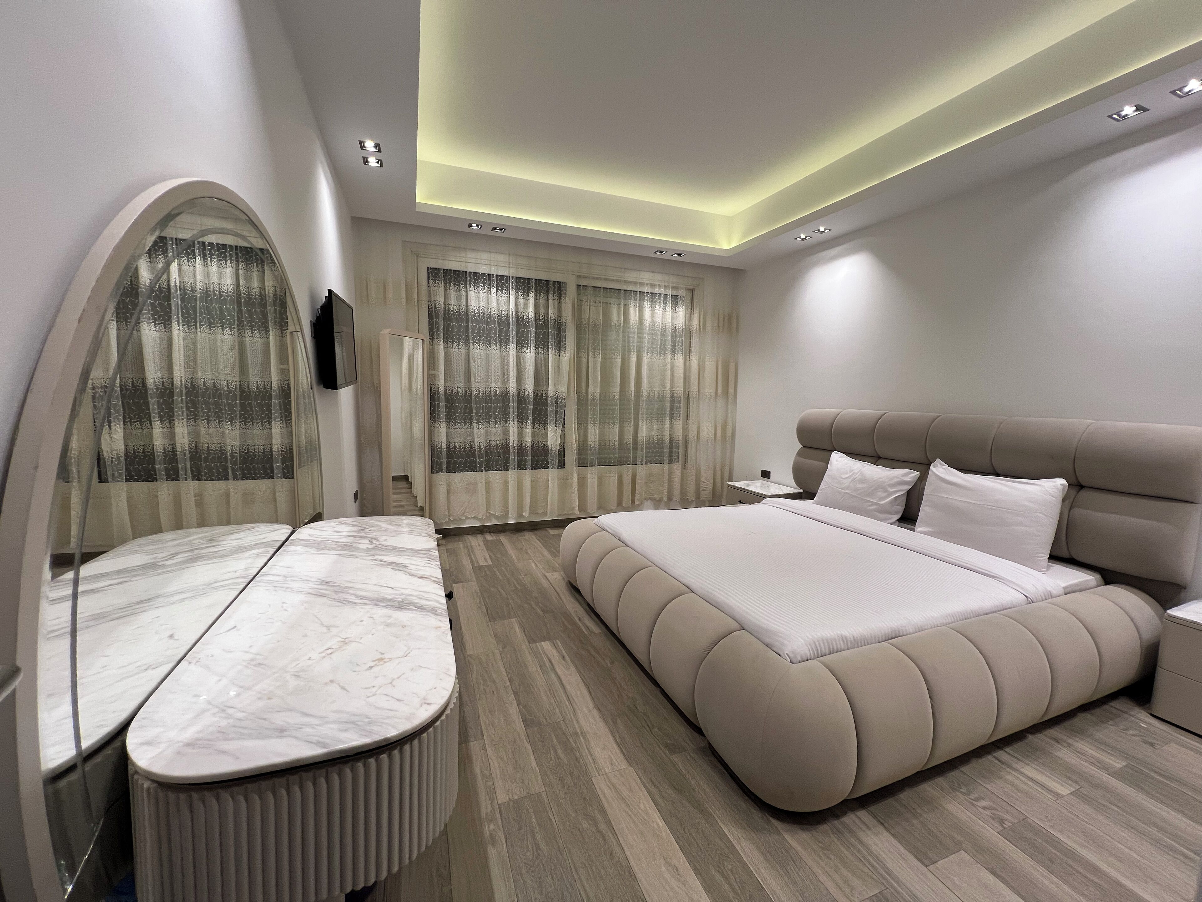 Ein modernes Schlafzimmer mit einem großen Bett, einem Marmor-Waschtisch und einem gebogenen Spiegel.