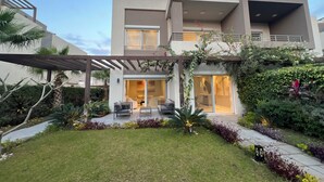 A modern two-story house with a patio area, outdoor seating, and lush landscaping. - ALSAWAH 5-Bedroom Villa with Private Pool  Palm Hills Sheikh Zayed (6th of October City)