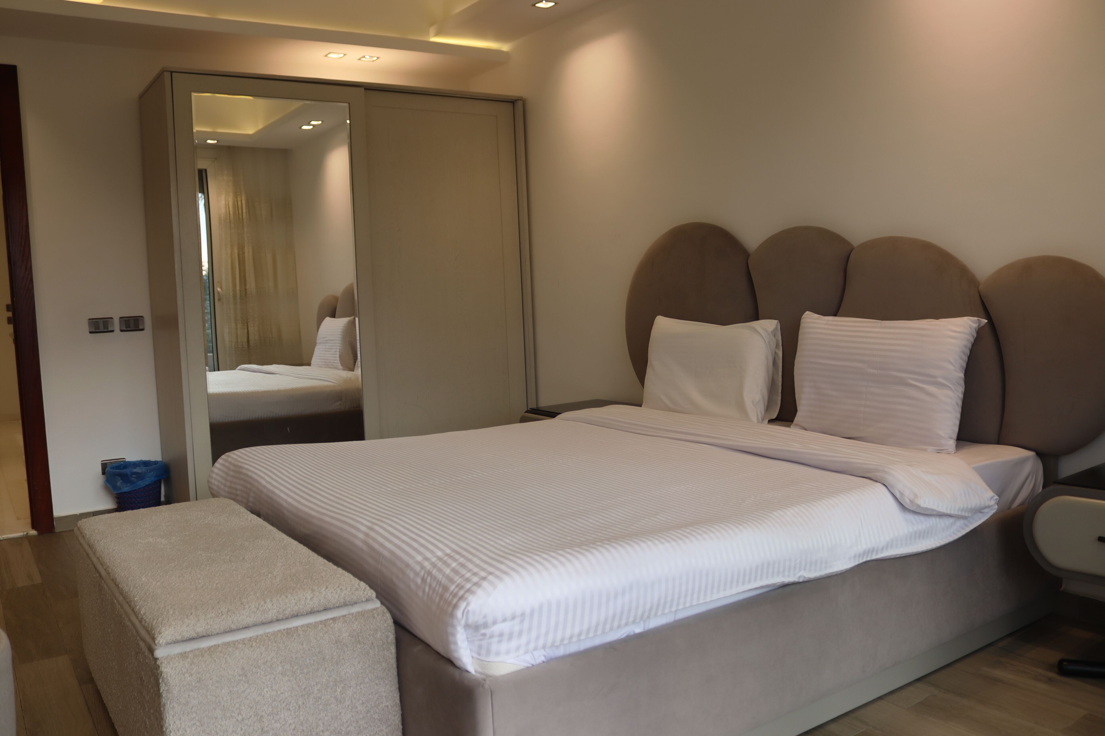 Quarto moderno com uma cama grande, uma mesinha de cabeceira e um espelho.