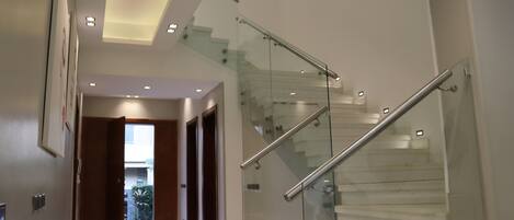 A modern interior with a glass staircase, a hallway leading to an outdoor area, and a door with a light switch.