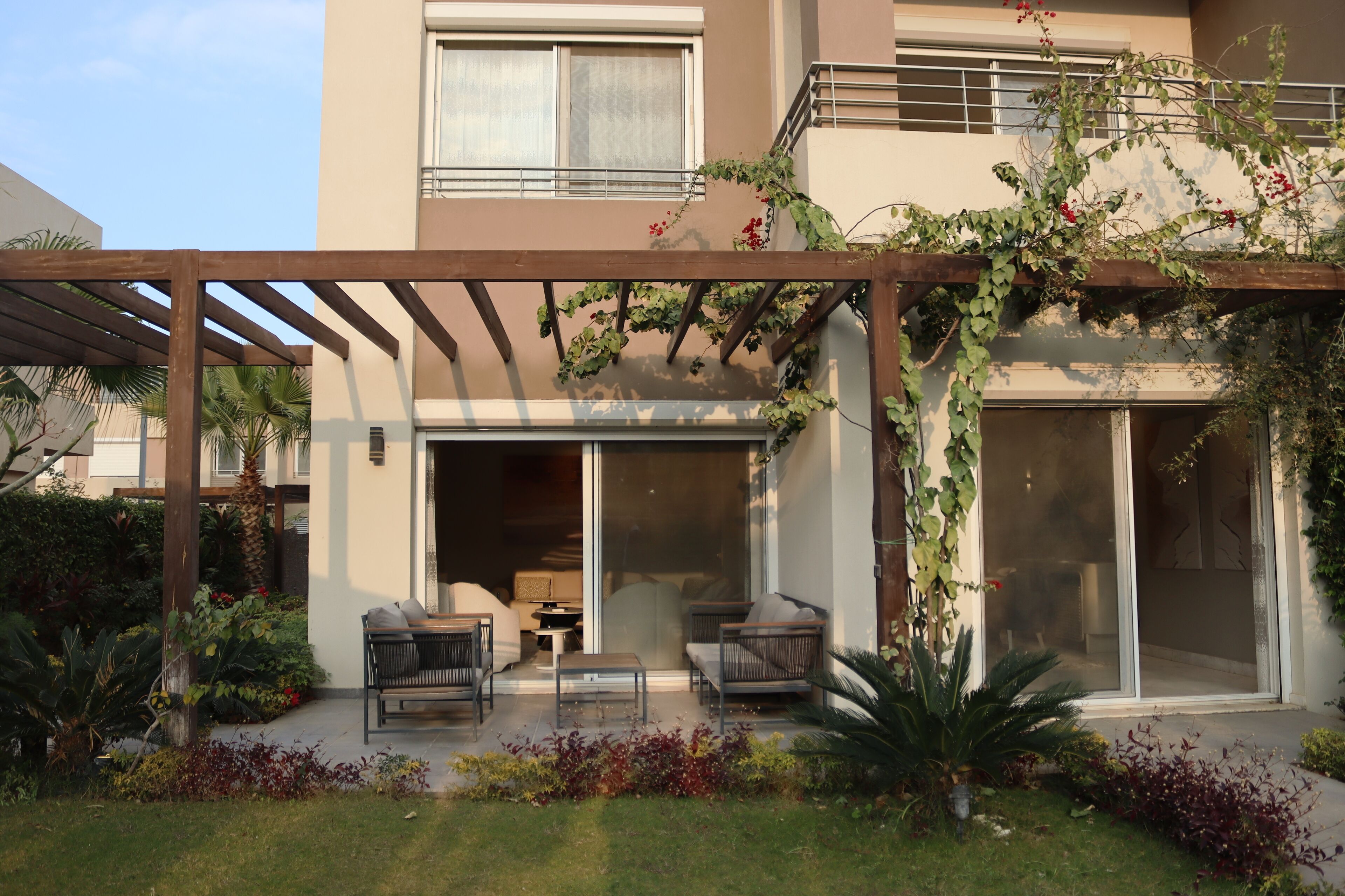 Une maison moderne dotée d’un patio couvert, d’un espace salon extérieur et d’une végétation luxuriante.