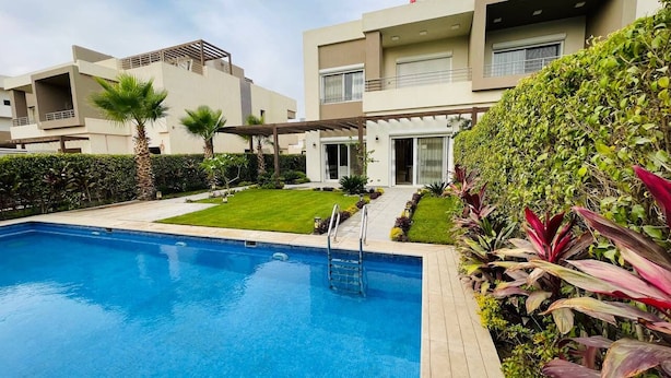 A modern pool area with a clear blue pool, a wooden deck, and a well-maintained lawn. - ALSAWAH 5-Bedroom Villa with Private Pool  Palm Hills Sheikh Zayed (6th of October City)