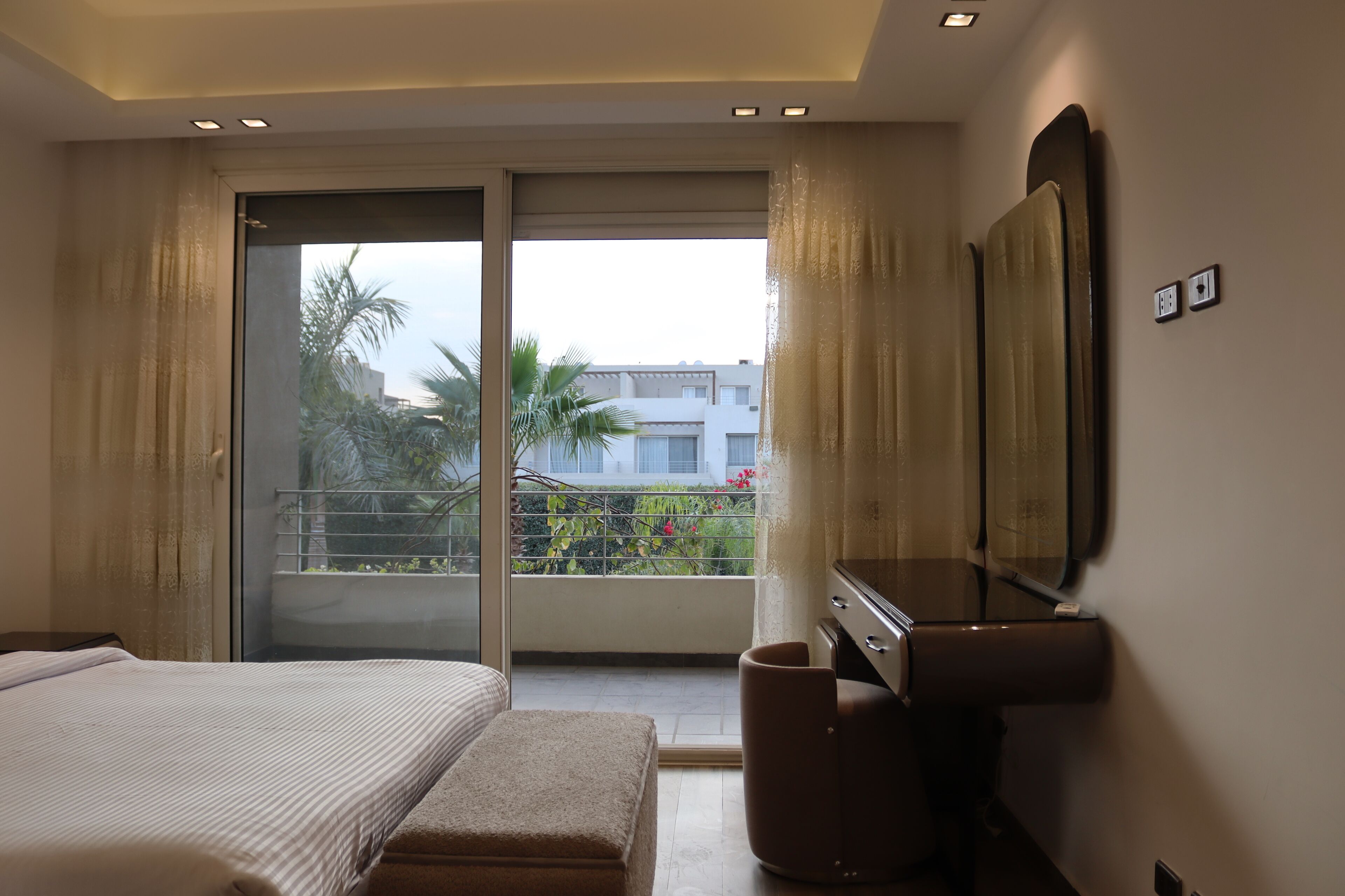 Une chambre d’hôtel moderne dotée d’un grand lit, d’un petit coin salon, d’un bureau et d’un balcon offrant une vue sur l’extérieur.