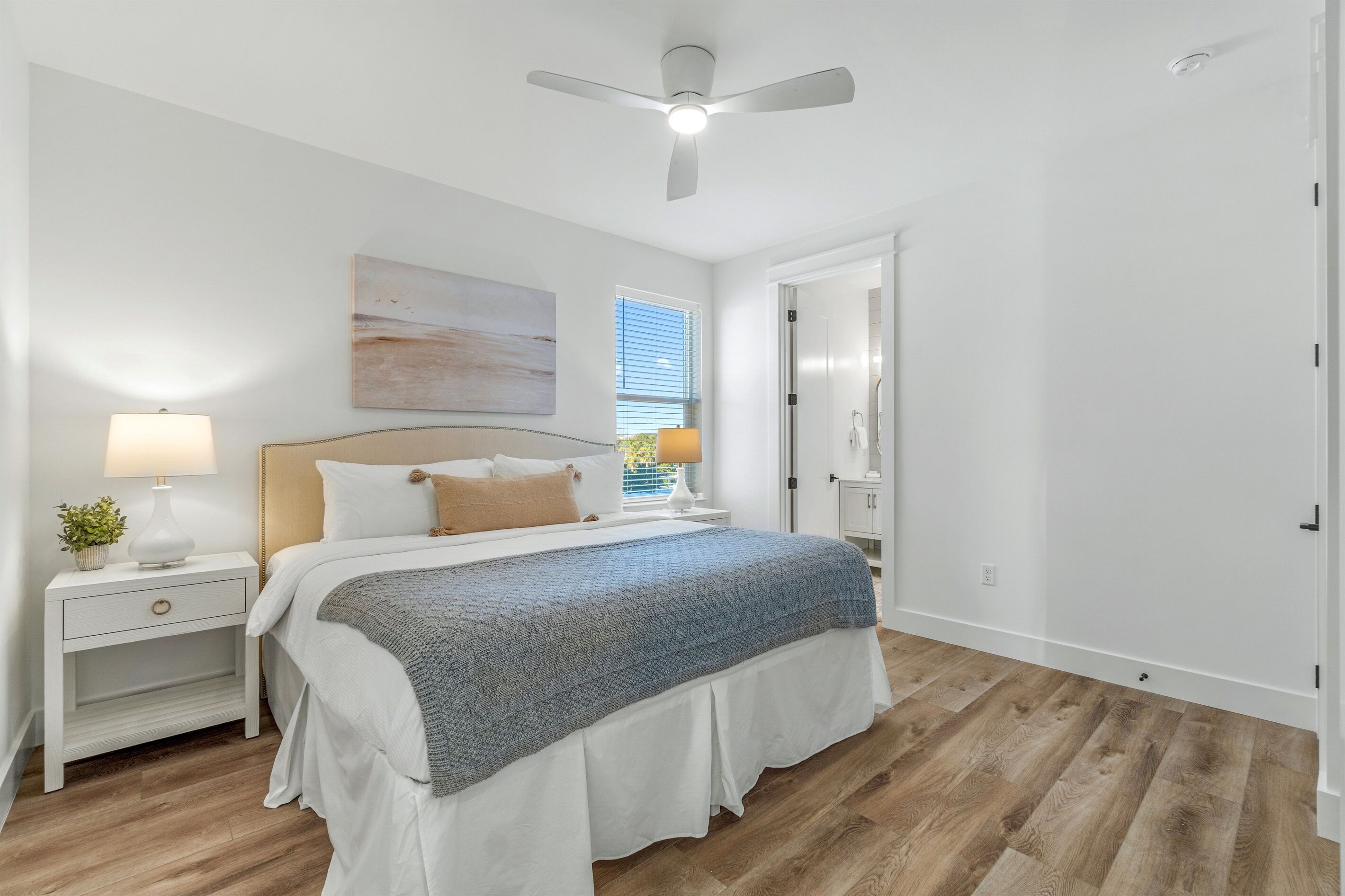 Un dormitorio con cama, mesitas de noche, ventilador de techo y una ventana con persianas.