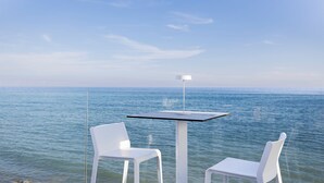 A table and two chairs by a glass railing with a view of the sea. - scirocco boutique eco hotel (Torre Pali)