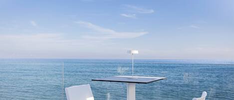 A table and two chairs by a glass railing with a view of the sea.