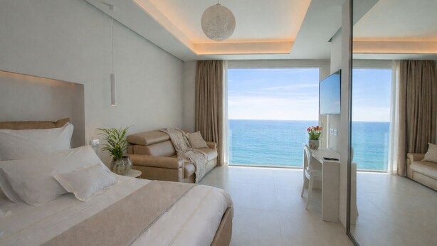 A modern hotel room with a large bed, a sofa, a desk, and a view of the ocean. - scirocco boutique eco hotel (Torre Pali)