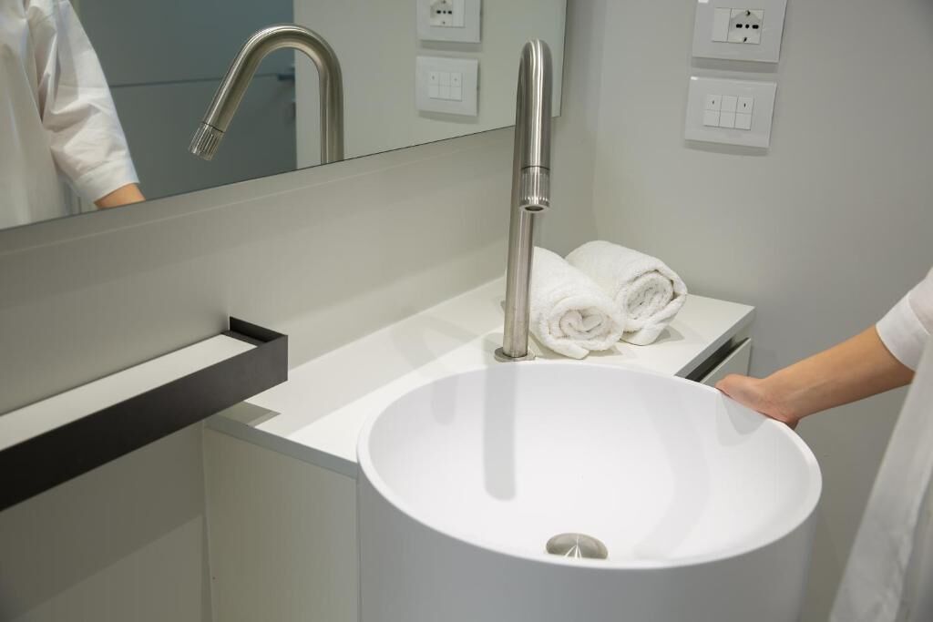 A modern bathroom with a white sink, a large mirror, and a towel rack.