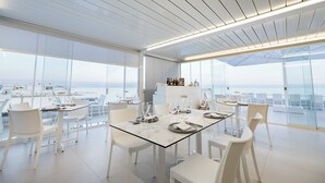 A modern dining area with glass tables and white chairs, large windows, and a view of the ocean. - scirocco boutique eco hotel (Torre Pali)