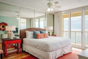 Ein Schlafzimmer mit einem großen Bett, einem Deckenventilator, einem Fernseher und Meerblick durch große Fenster.