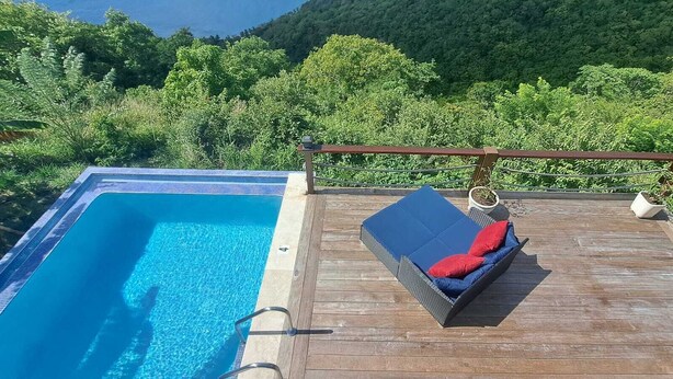 Eine Holzterrasse mit Pool und Liegestuhl mit roten Kissen.