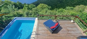 A wooden deck with a pool and a lounge chair with red cushions. - Sunset Hideaway is one of the most breathtaking locations in all of St. Lucia. (Choiseul)